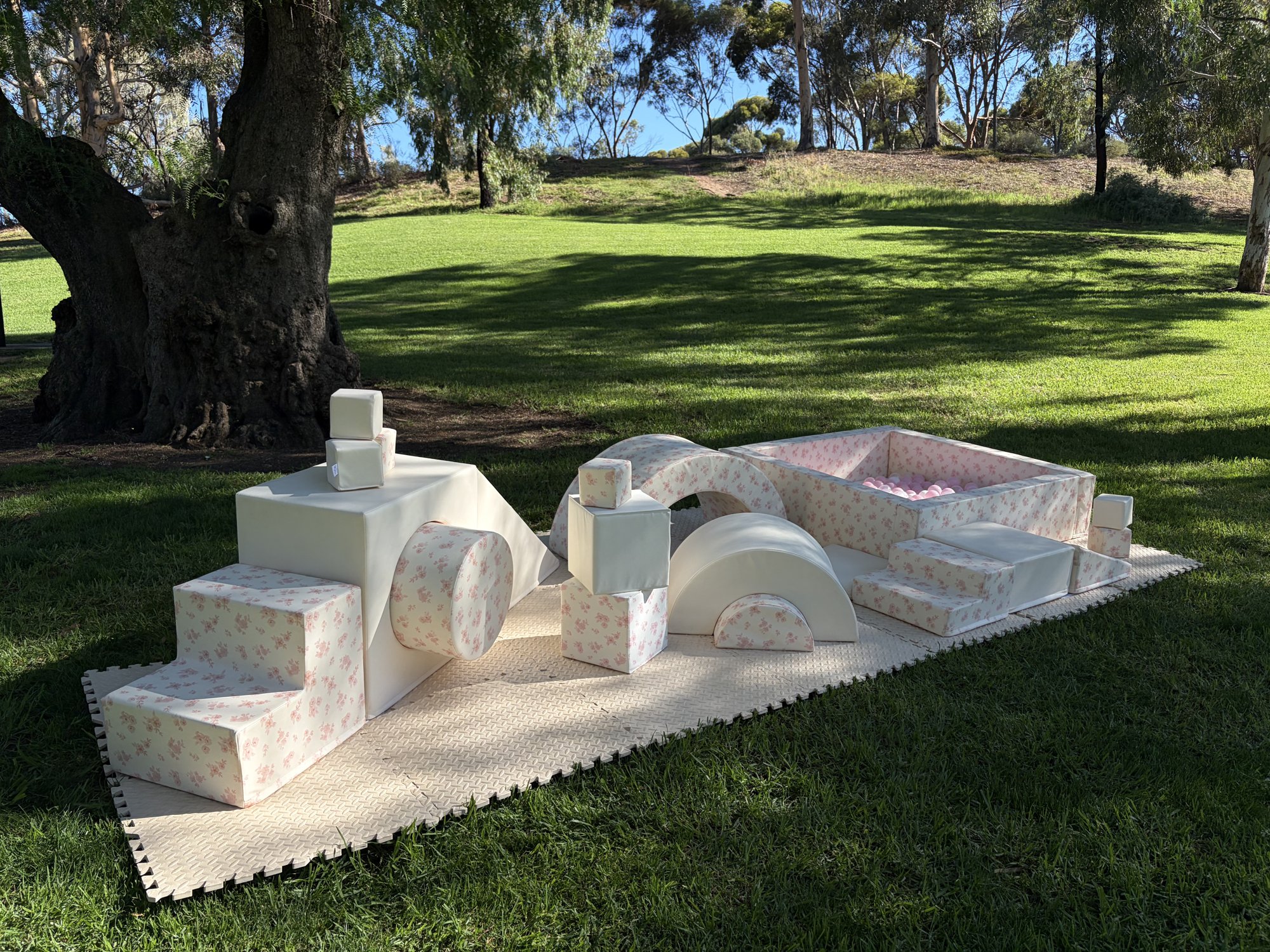 Pink floral soft play setup with ball pit, blocks and arches set up outdoors under a gum tree in a Barossa park.