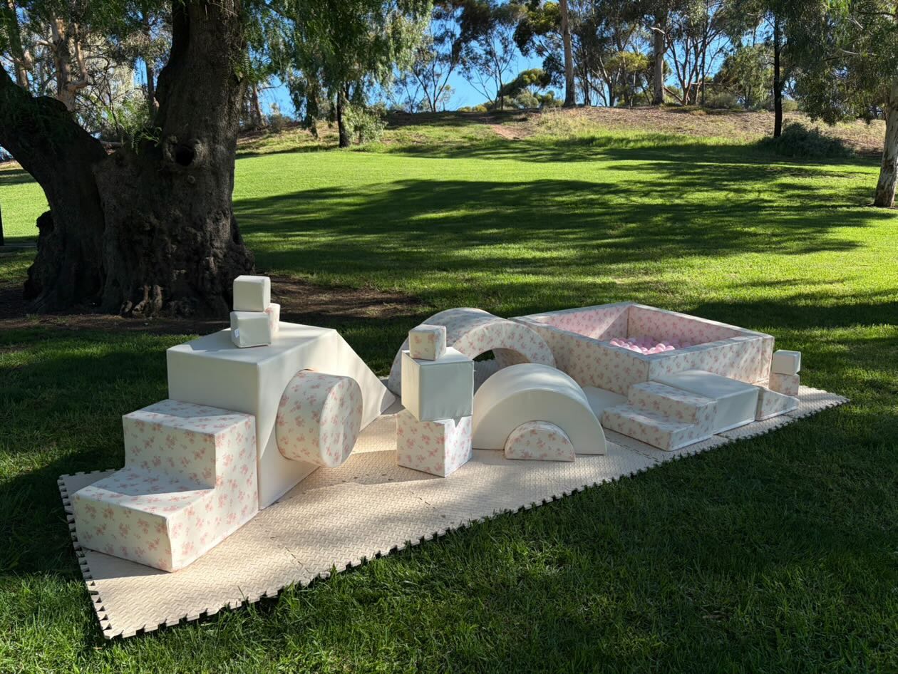 Pink floral soft play setup with ball pit and arches set up outdoors under a tree in a Barossa park.